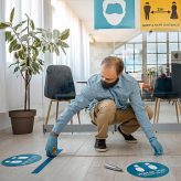 Hombre colocando señales en el piso para el distanciamiento social en una oficina.