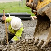Worker using a small tracked excavator to dig a hole to fix a water leak at a large commercial housing development in Oregon