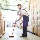 Warehouse worker working in warehouse, sweeping the floor. About 30 years old, Caucasian male.
