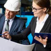 Portrait of senior businessman looking at floor plans of modern factory with young assistant manager explaining the construction